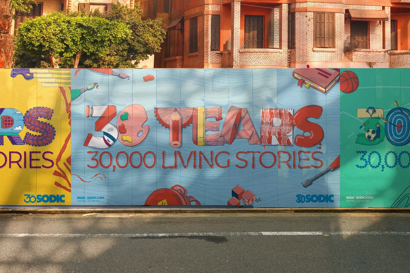 SODIC blue education anniversary poster on a street wall with red brick buildings behind it
