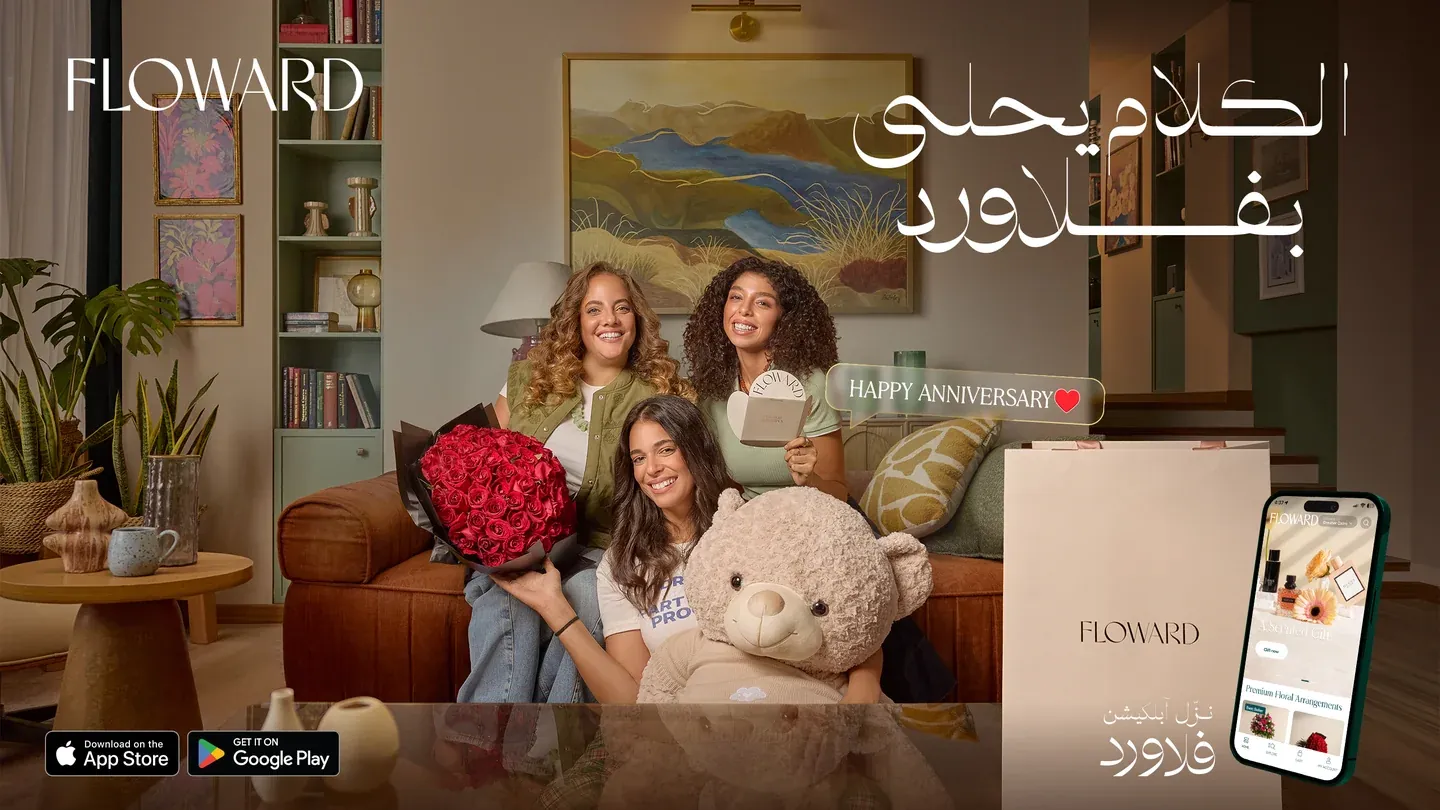 Floward anniversary artwork with women, a red bouquet, gifts and a large teddy bear in a living room